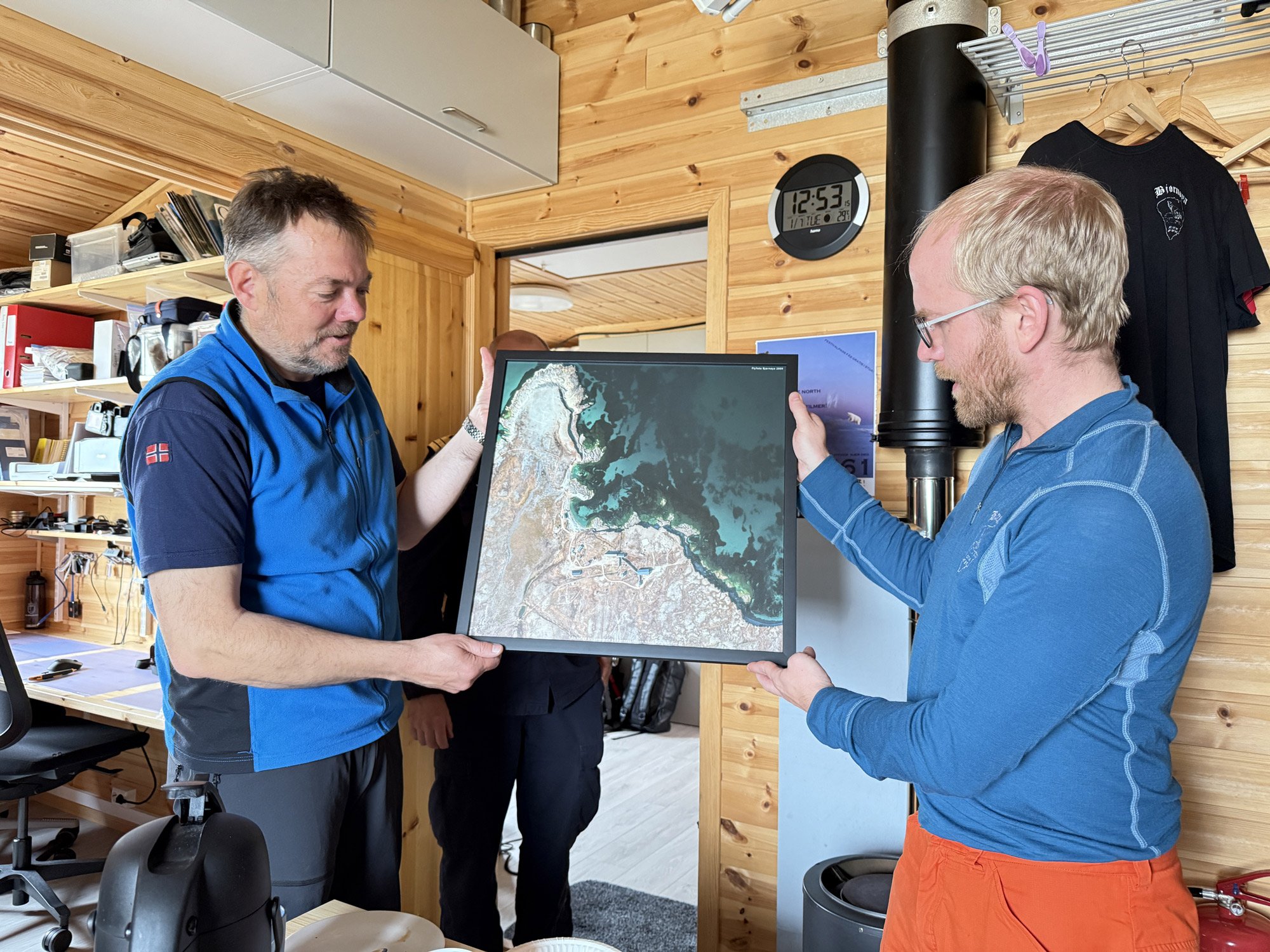 Et innrammet foto blir overrakt mellom to menn i turklær i et arbeidsværelse