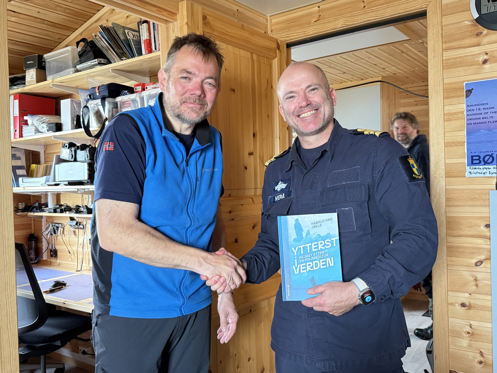En bok blir overrakt mellom to menn i et arbeidsværelse