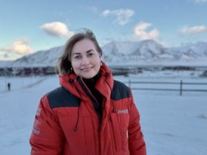 Kvinne i rød jakke med fjell i bakgrunnen