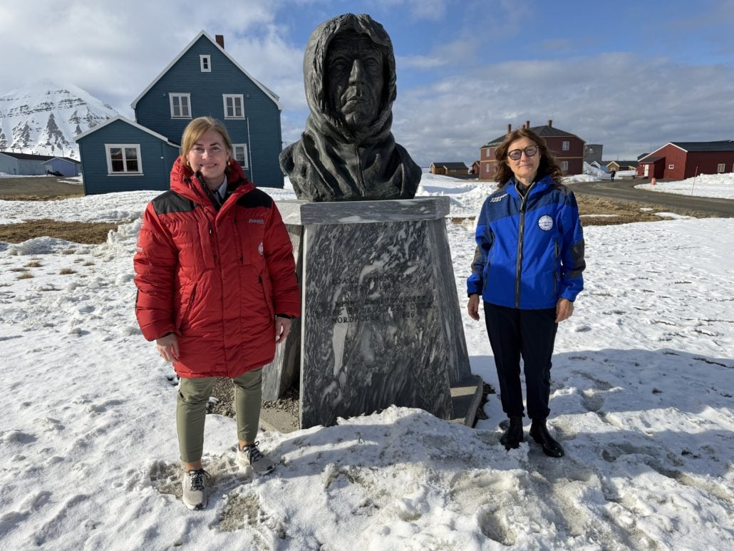 To kvinner står på hver sin side av en byste av Roald Amundsen
