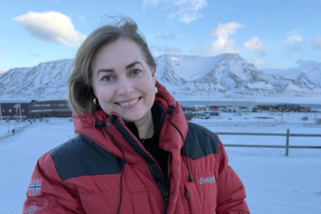 Kvinne i rød jakke med snøkledde fjell i bakgrunnen.