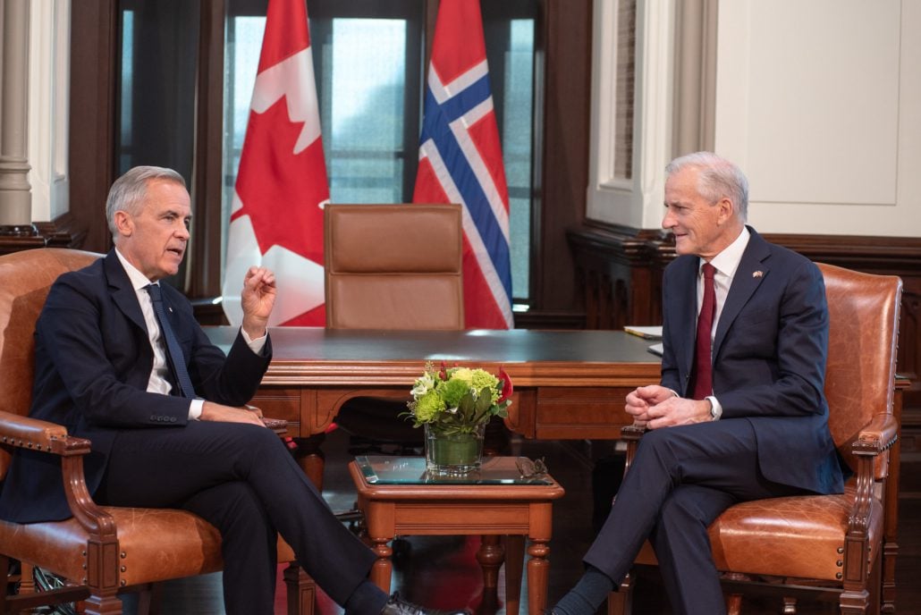 To personer snakker sammen med et canadisk og et norsk flagg i bakgrunnen.
