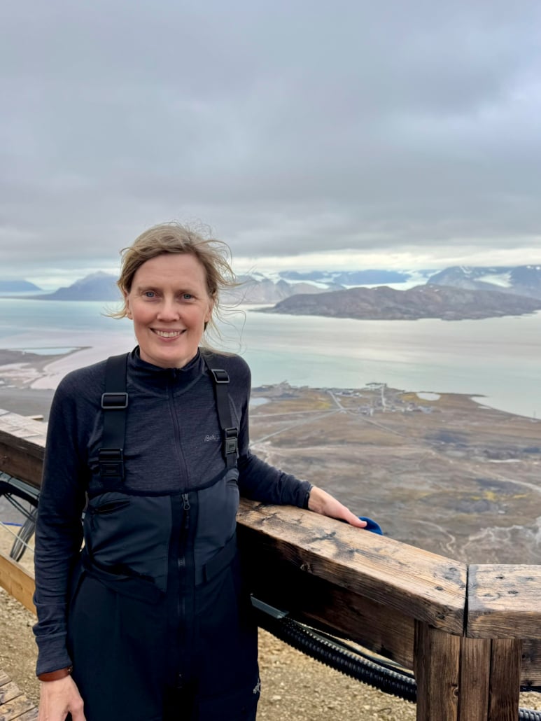 Person står foran en fjord og snøkledde fjell