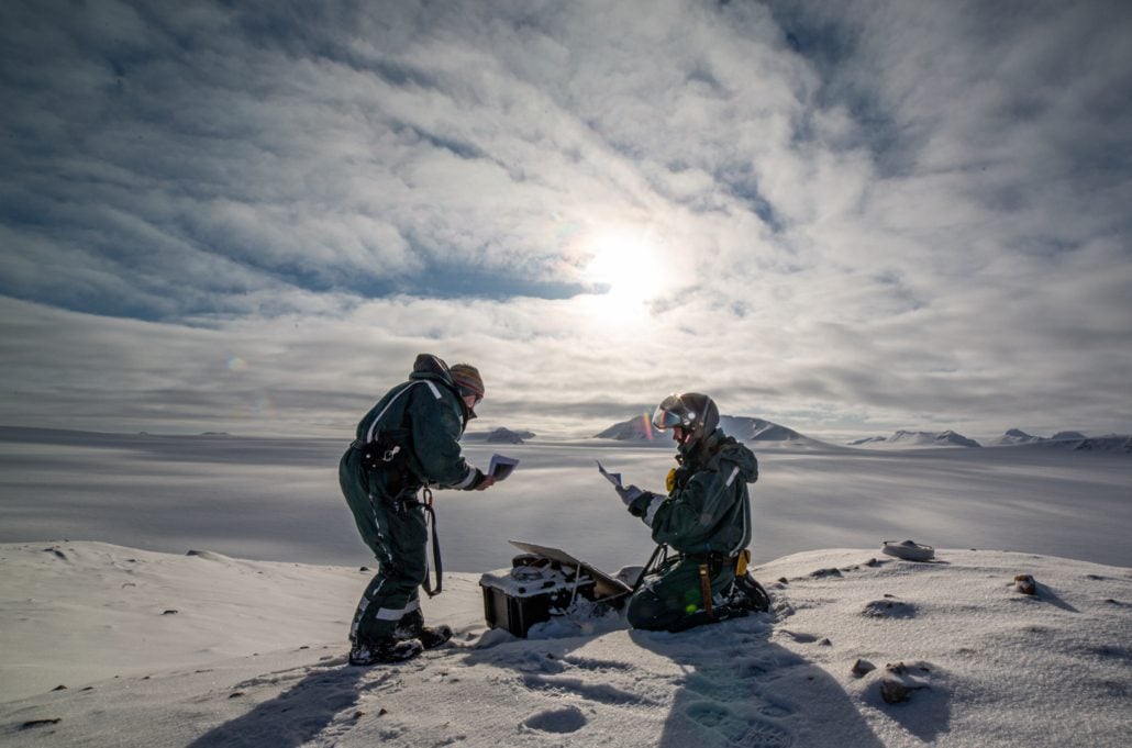 to personer gjør målinger på snødekket fjell